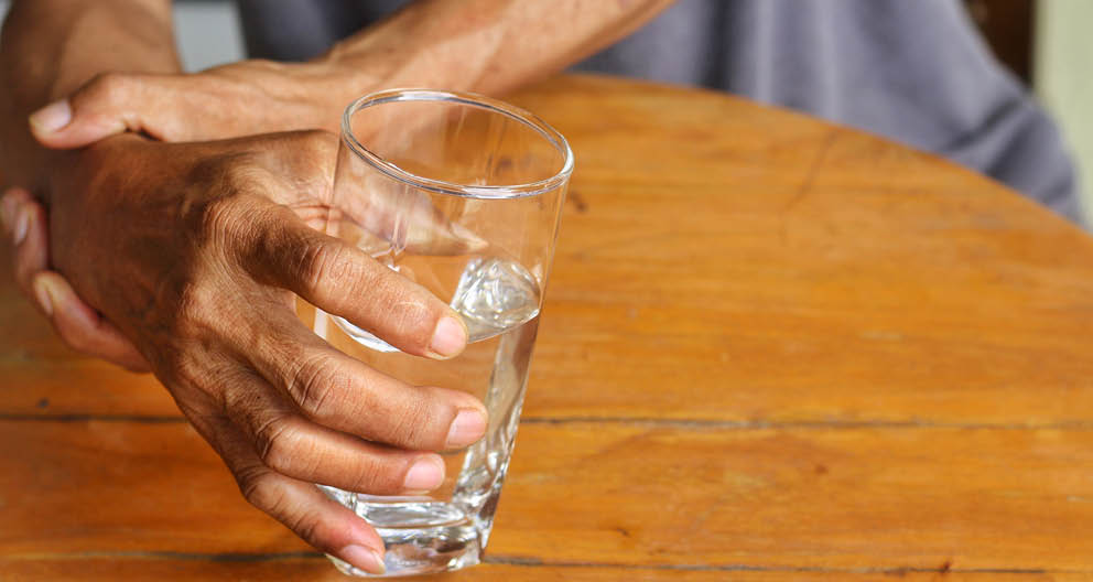Elderly man is holding his hand while drinking water because Parkinson's disease Tremor is most symptom and make a trouble for doing activities such as eat or drink Health care or elderly concept 