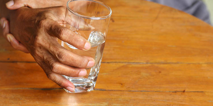 Elderly man is holding his hand while drinking water because Parkinson's disease Tremor is most symptom and make a trouble for doing activities such as eat or drink Health care or elderly concept 