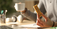 Photo of someone with a cereal bar in one hand and a cup in the other